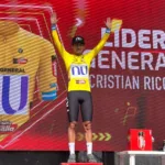 Cristian Rico en el podio de la Vuelta a Guatemala 2026 con el maillot amarillo de líder y una gorra del NU Colombia.